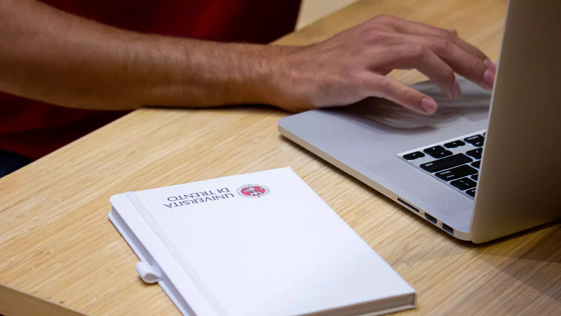 mani che digitano su tastiera laptop, agenda con logo UniTrento