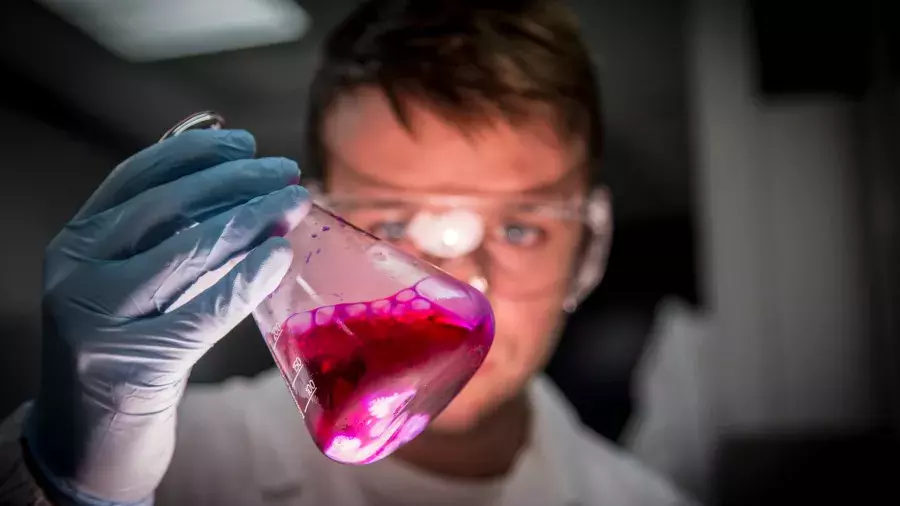provetta con liquido fucsia, volto di ricercatore
